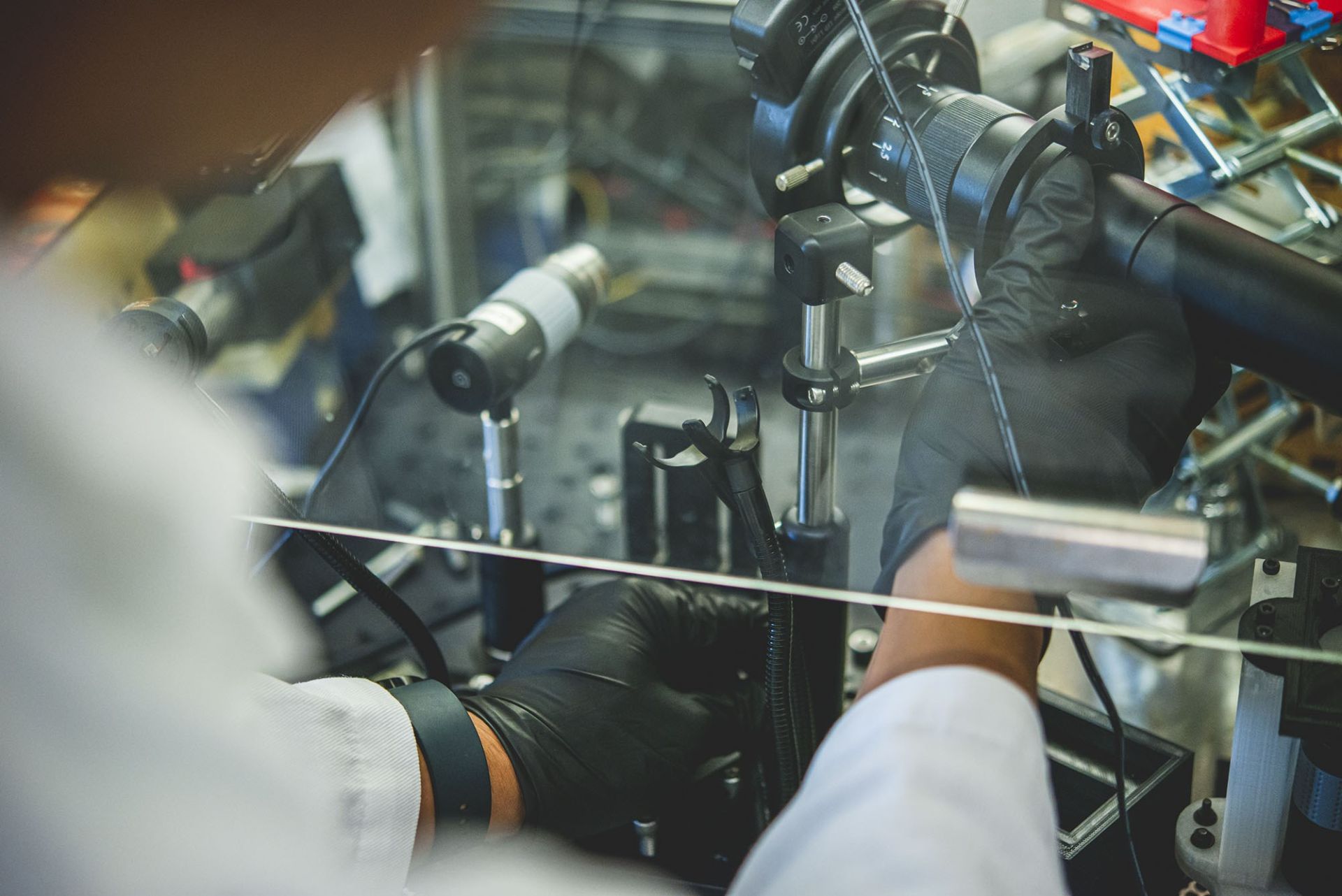 Person wearing white lab coat and black latex gloves adjusts machine parts of a bioprinter.