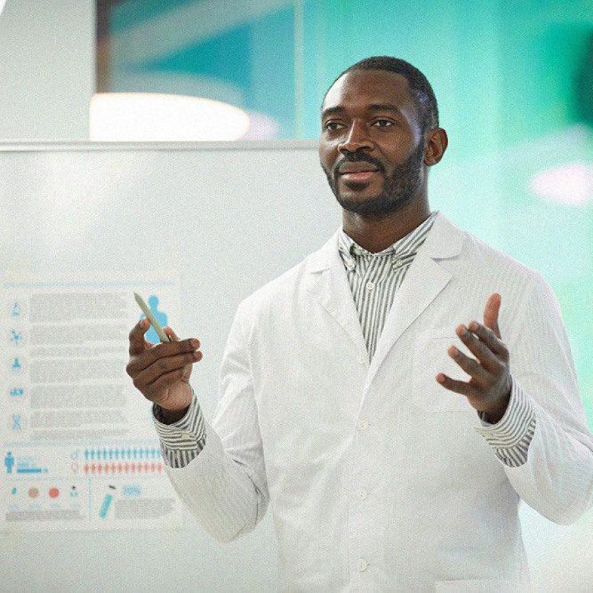 Black man in white lab coat giving a lecture.